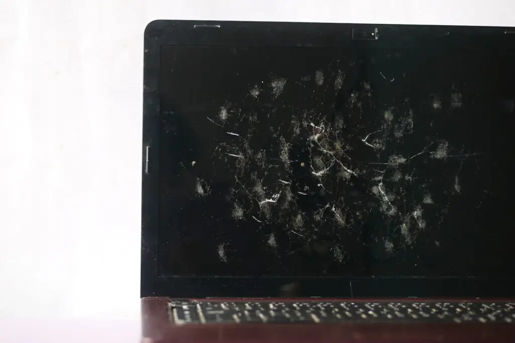 Severe cracked laptop screen with multiple impact points and scratches, in need of professional repair.